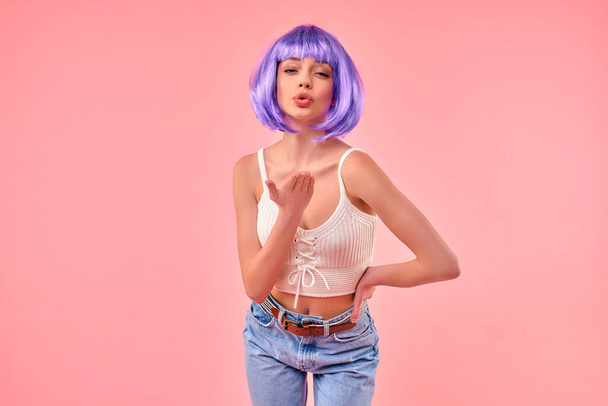Krásná mladá sexy dívka v fialové paruce posílá vzdušný polibek izolované na růžové pozadí. - Fotografie, Obrázek