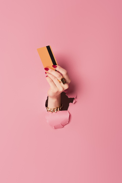 Rajatut näkymä nainen punainen manikyyri tilalla luottokortti lähellä vaaleanpunainen tausta reikä  - Valokuva, kuva