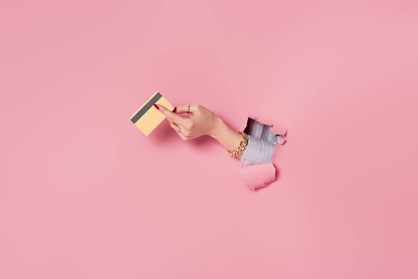 Partial view of credit card in hand of woman near pink background with hole  - Foto, Imagem