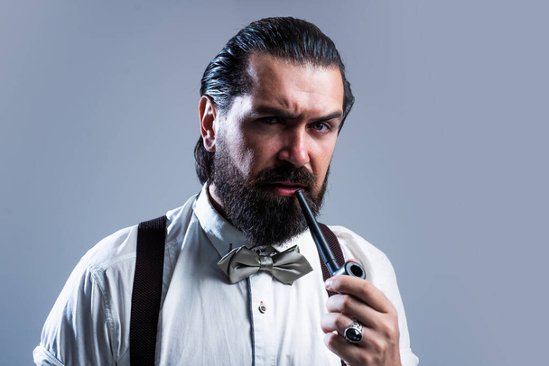 elegant brutal man in formal wear has groomed hair smoking pipe, addiction - 写真・画像