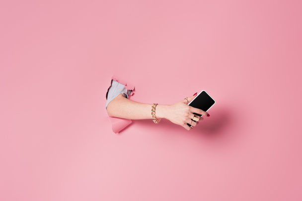 Rajatut näkymä nainen matkapuhelin lähellä vaaleanpunainen tausta reikä  - Valokuva, kuva