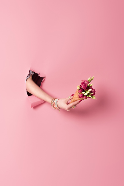 Cropped view of waffle cone with flowers in hand of woman in hole of pink background  - Photo, Image