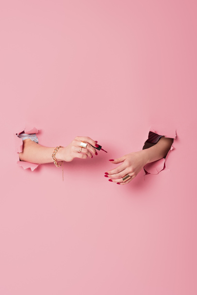 Partial view of woman applying nail polish near pink background with holes  - Fotó, kép