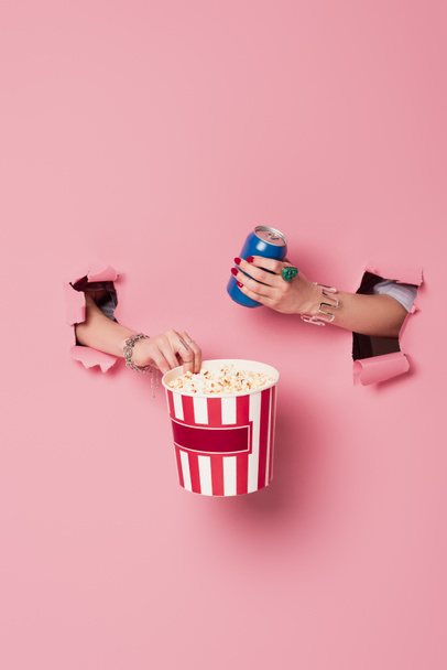 Cropped view of woman holding popcorn and drink in can near pink background with holes  - Photo, Image