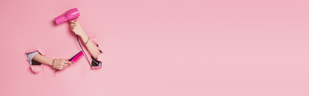 Vista recortada de secador de pelo y peine en las manos mujer cerca de fondo rosa con agujeros, pancarta  - Foto, Imagen