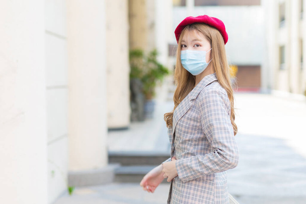 長い青銅の髪のアジアの女性は、灰色のスーツを着て街を歩き、新しい通常のライフスタイルで医療面マスクを身に着けています. - 写真・画像