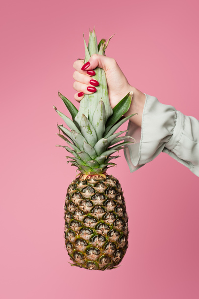 Partial view of woman holding tropical pineapple isolated on pink  - Фото, изображение