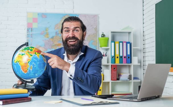 Male teacher in the classroom teaching geography pointing to a world map, education - Фото, изображение