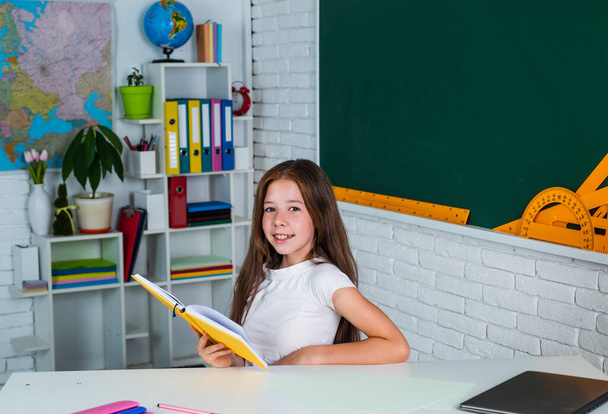 smiling teen girl reading book in school classroom, education - Фото, изображение