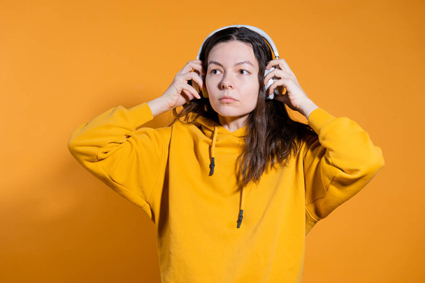 Music lovers enjoy music. A young woman in a yellow hoodie with white wireless headphones, - Photo, Image