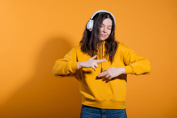Happy dancing music lover. A young woman in a yellow hoodie with white wireless headphones, - Foto, immagini