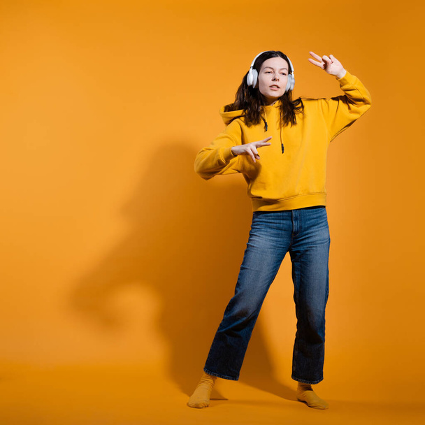 Happy dancing music lover. A young woman in a yellow hoodie with white wireless headphones, - Foto, Imagen