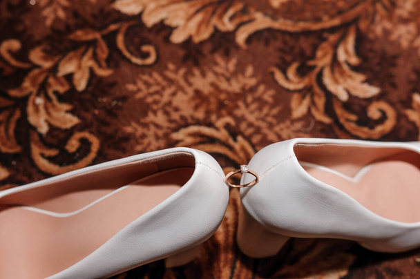 Morsiamen valkoiset kengät ja vihkisormus ruskealla taustalla. Häät tarvikkeet - Valokuva, kuva