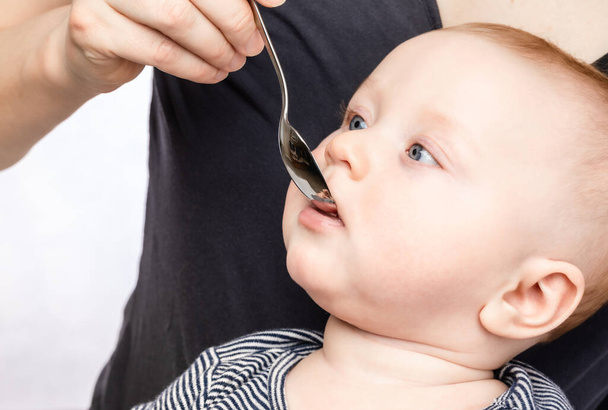 Mother feeding baby boy with vitamin or liquid medicine using spoon - Φωτογραφία, εικόνα