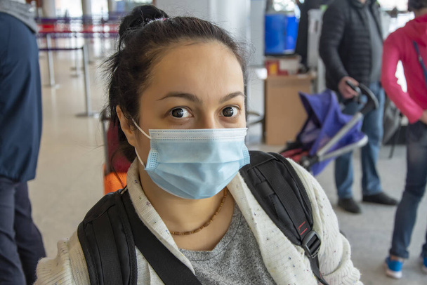 Portrét 35-40-leté ženy v lékařské masce a kontaktních čočkách na letišti, odbavení pro odjezd ze země, osoby s taškami a kufry. - Fotografie, Obrázek