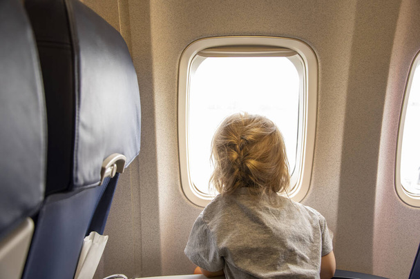 Das Mädchen blickt aus dem Fenster des Flugzeugs auf die Wolken. - Foto, Bild