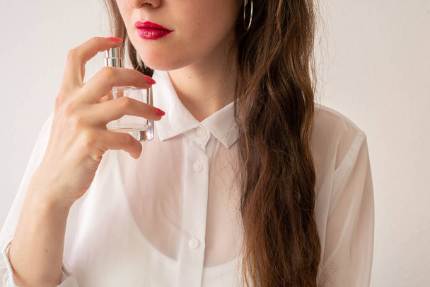 uma menina em uma elegante blusa branca e com uma manicure rosa segura um frasco de perfume delicado - Foto, Imagem