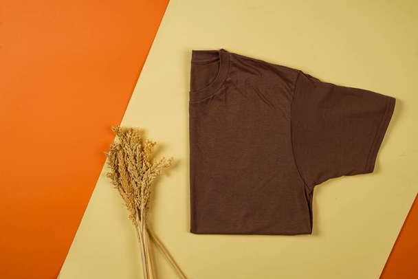 Plain brown t-shirt isolated on orange and yellow background adds to the bright impression. T-shirts made of cotton are very comfortable for everyday wear. Empty space for your ad. T-shirt mockup. - Photo, Image
