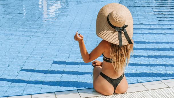 Летний концептуальный фон. Счастливая молодая сексуальная девушка в купальнике бикини, солнцезащитных очках и соломенной шляпе в голубой воде бассейна. Курортный спа в отеле на отдыхе - Фото, изображение