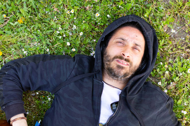 Hippy férfi feküdt szakállal és fejhallgató gitározik a szabadban a füvön - Fotó, kép