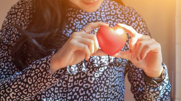 Egy ázsiai nőnek van egy piros szív szimbóluma, amit odaadhat a szeretőjének Valentin-napon, hogy megmutassa a szeretetét és a barátságát, ami mindig is. - Fotó, kép