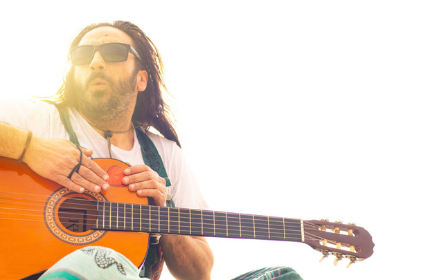 Хиппи с бородой и в очках играет на гитаре на пляже - Фото, изображение
