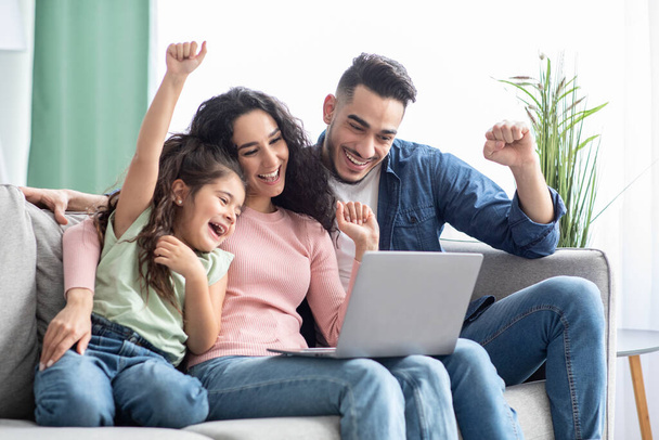 Счастливая арабская семья из трех человек празднует успех с ноутбуком дома - Фото, изображение