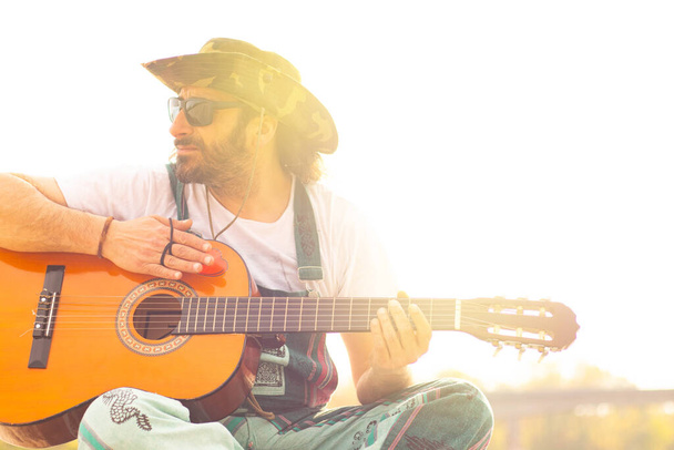 Hippy man with hat beard and glasses playing guitar outdoors on the beach - Valokuva, kuva