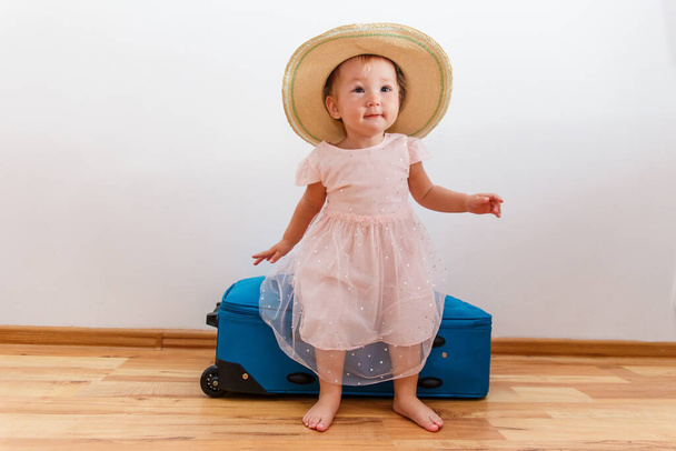 one-year-old girl in a hat and suitcase indoors - Foto, afbeelding