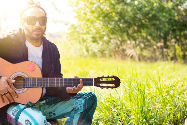 Хиппи с бородой и в очках играет на гитаре на траве - Фото, изображение