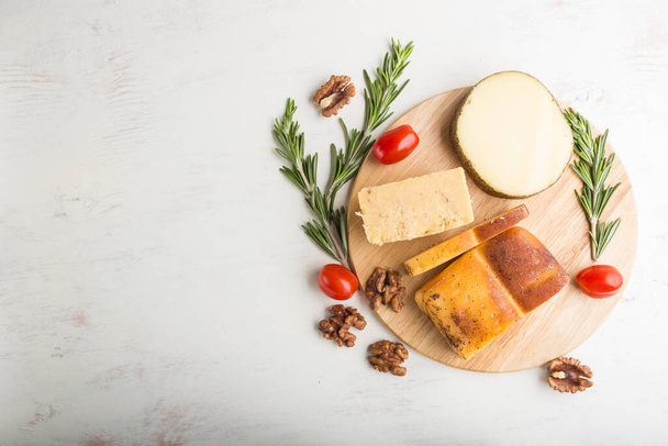 Gerookte kaas en verschillende soorten kaas met rozemarijn en tomaten op houten plank op een witte houten achtergrond. Bovenaanzicht, flat lay, kopieerruimte. - Foto, afbeelding