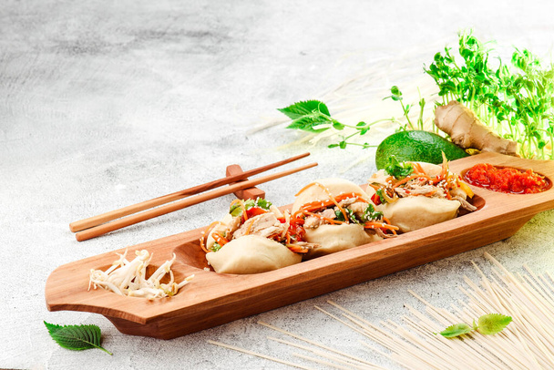 Cibo tradizionale pan-asiatico. Bao - torta al vapore con ripieno di carne e verdure fresche su piatto di legno con bacchette cinesi. Sfondo concreto. Spazio per testo - Foto, immagini
