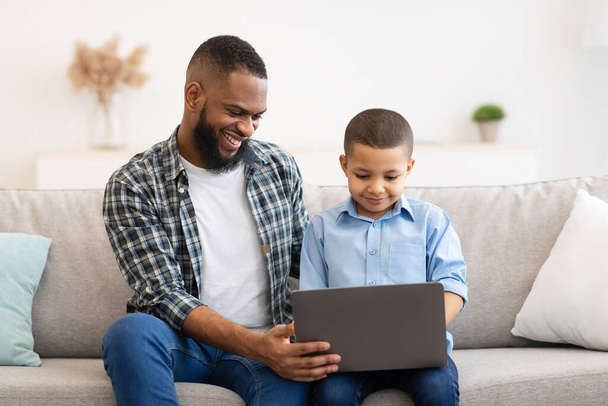アフリカ系アメリカ人の少年と彼の父親が自宅でノートパソコンを使う - 写真・画像