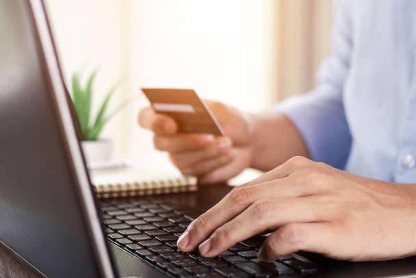 Biznesmen ręka trzymając kartę kredytową z wykorzystaniem laptopa do zakupów online podczas składania zamówień w domu. biznes, styl życia, technologia, handel elektroniczny, bankowość cyfrowa i koncepcja płatności online. - Zdjęcie, obraz