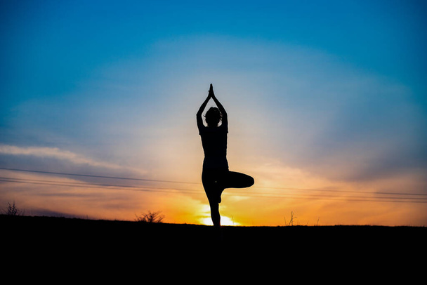 woman in a balancing pose at sunset yoga outdoors - Photo, Image