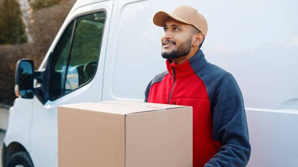 Smiling bearded delivery man wearing beige cap looking away - Фото, изображение