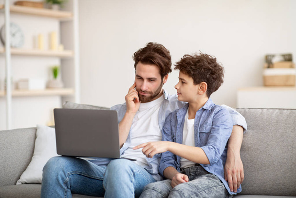 Teini-ikäinen poika selittää isä miten käyttää kannettavaa tietokonetta, surffata internetissä ja pelaa peliä. Perhe viettää aikaa yhdessä, - Valokuva, kuva