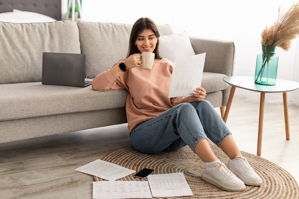 Señora sosteniendo el informe de lectura de papel bebiendo café en casa - Foto, Imagen