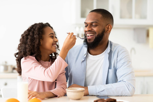 Cheerful african daughter feeding father with cereal - Foto, immagini