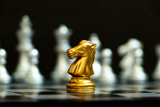Chevalier d'or dans le jeu d'échecs face à l'autre équipe d'argent sur fond noir (Concept pour la stratégie de l'entreprise, la victoire ou la décision d'affaires) - Photo, image