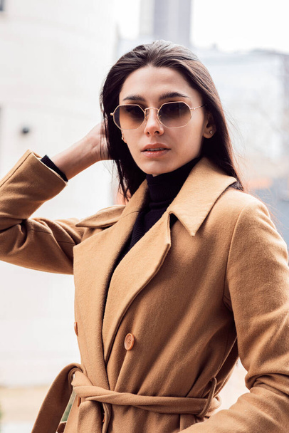 Stylish portrait of a beautiful young woman in sunglasses and a brown coat outdoors - Foto, afbeelding