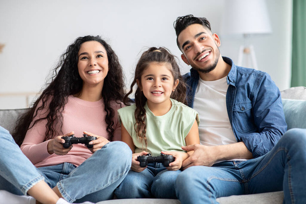 Allegra famiglia mediorientale con piccola figlia che gioca ai videogiochi a casa - Foto, immagini