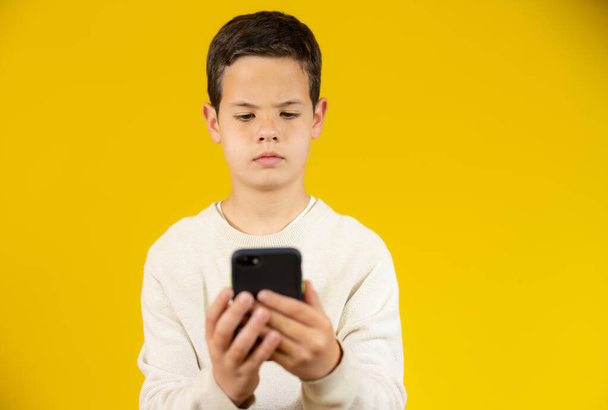 Lindo chico usando el teléfono móvil aislado sobre fondo amarillo. - Foto, imagen