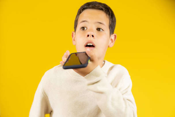 Cute boy mówi przez telefon komórkowy izolowane na żółtym tle. - Zdjęcie, obraz