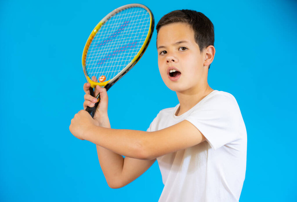 Молодий хлопчик з тенісною ракеткою ізольований на синьому фоні
. - Фото, зображення
