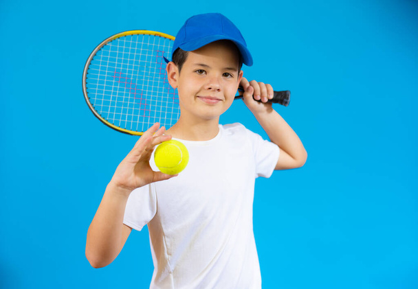 Niño con raqueta de tenis y pelota aislada sobre fondo azul. - Foto, Imagen