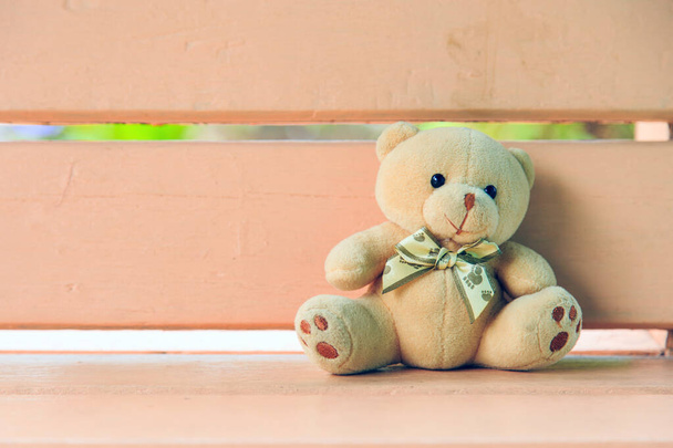 Ein alter Teddybär sitzt auf einer hellen, pfirsichfarbenen Holzbank, links ist Platz für Kopien - Foto, Bild
