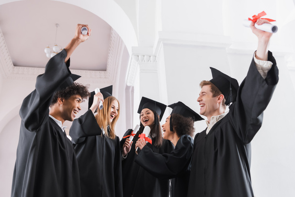 Radosni, wieloetniczni absolwenci z dyplomami na uniwersytecie  - Zdjęcie, obraz