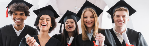 Estudiantes multiétnicos en gorras con diplomas y sonriendo a la cámara, pancarta  - Foto, Imagen