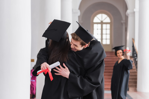 Graduado sonriente con un amigo abrazador de diploma  - Foto, imagen